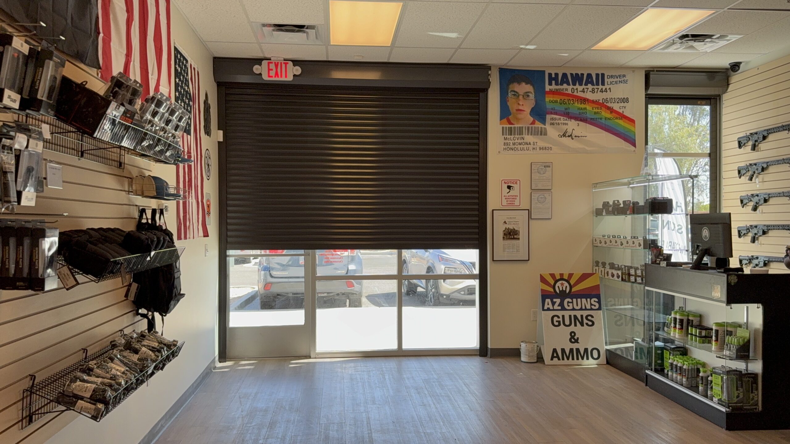 Interior of a shop featuring firearms accessories on display shelves, an entrance with a roll-up door, and a sign that reads 'AZ GUNS & AMMO'. There are also American flags on the wall and promotional materials visible.