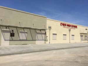The exterior of Cypher High School, featuring a light-colored building with closed shutters. The school's name is displayed in bold red letters above the entrance, under a clear blue sky.