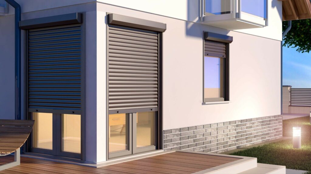 A modern house exterior with closed roller shutters over the windows, a wood deck in front, and a small balcony above the white wall.